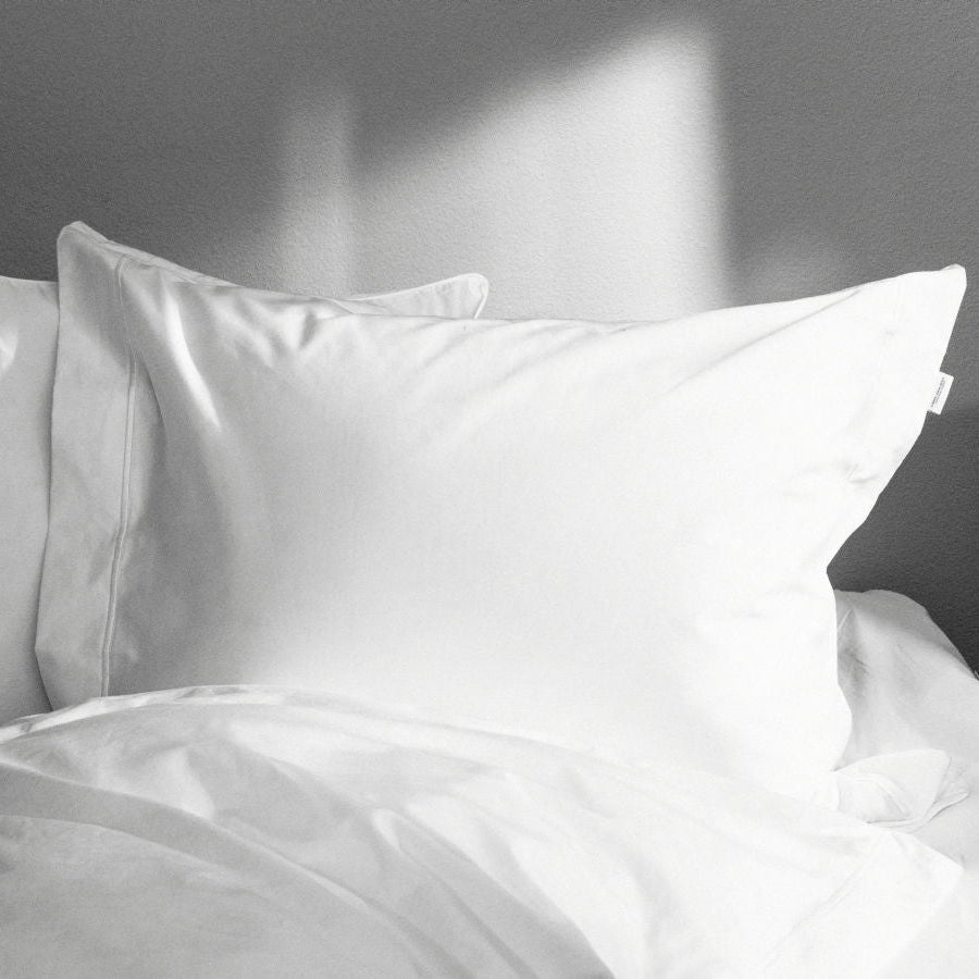 White satin pillowcases on a bed with a neutral background