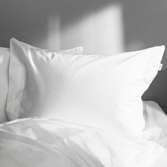 White satin pillowcases on a bed with a neutral background